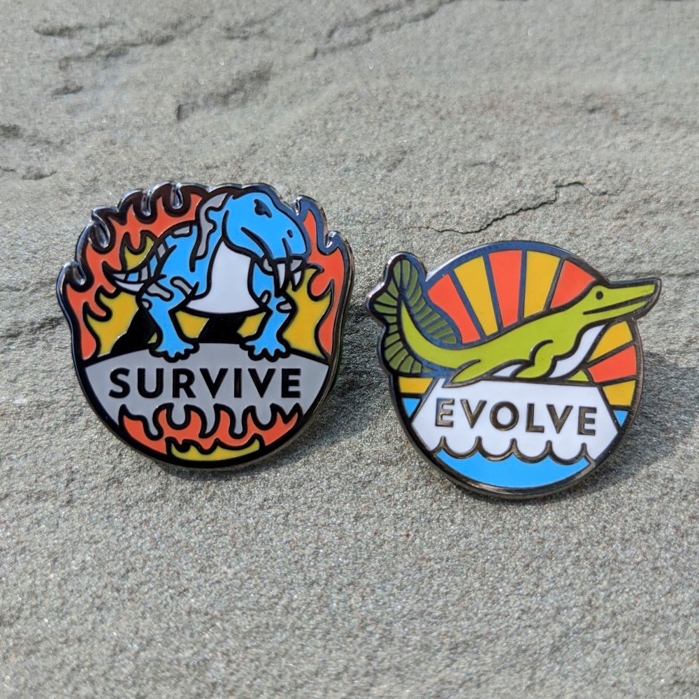 Two enamel pins. One is a lystrosaurus emerging from flames with the text "survive" underneath. The other is a tiktaalik perched on a pedestal above water with sunrise beams behind it and the text "Evolve."