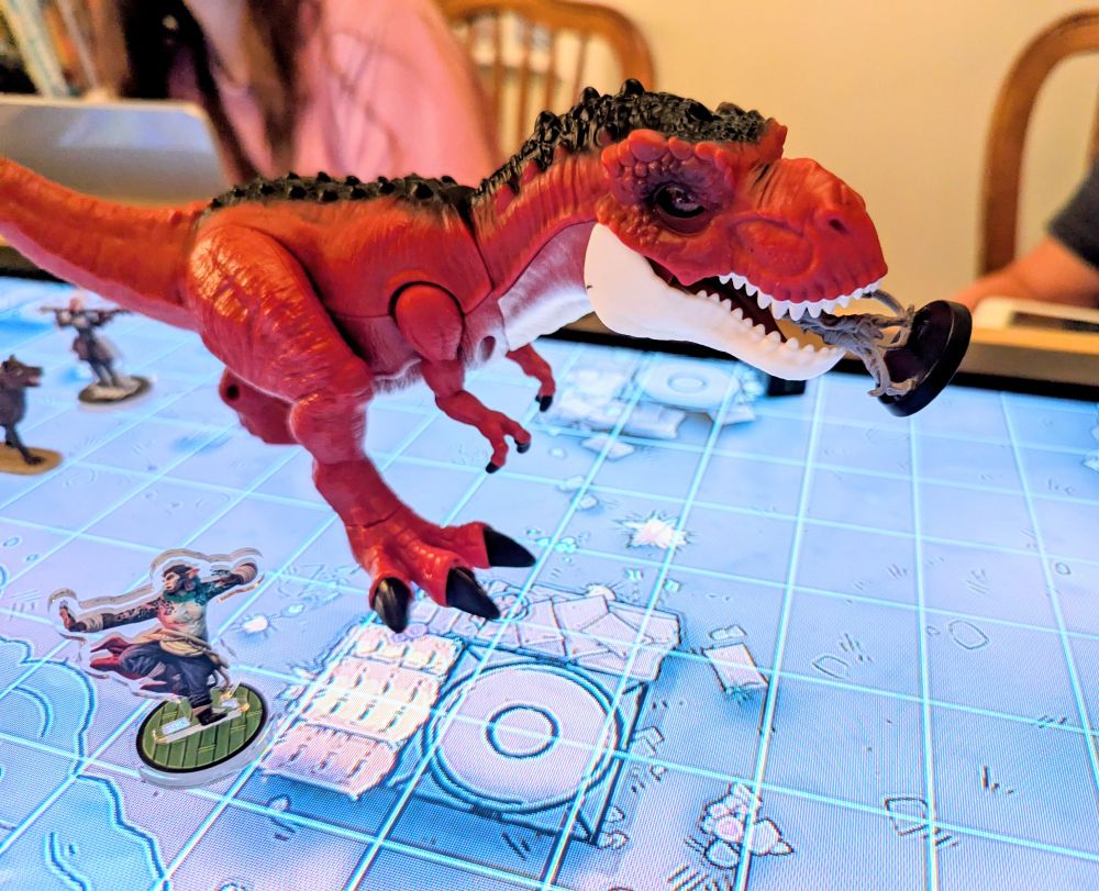 A D&D map with miniatures and a toy T-Rex with one of the miniatures in its mouth.