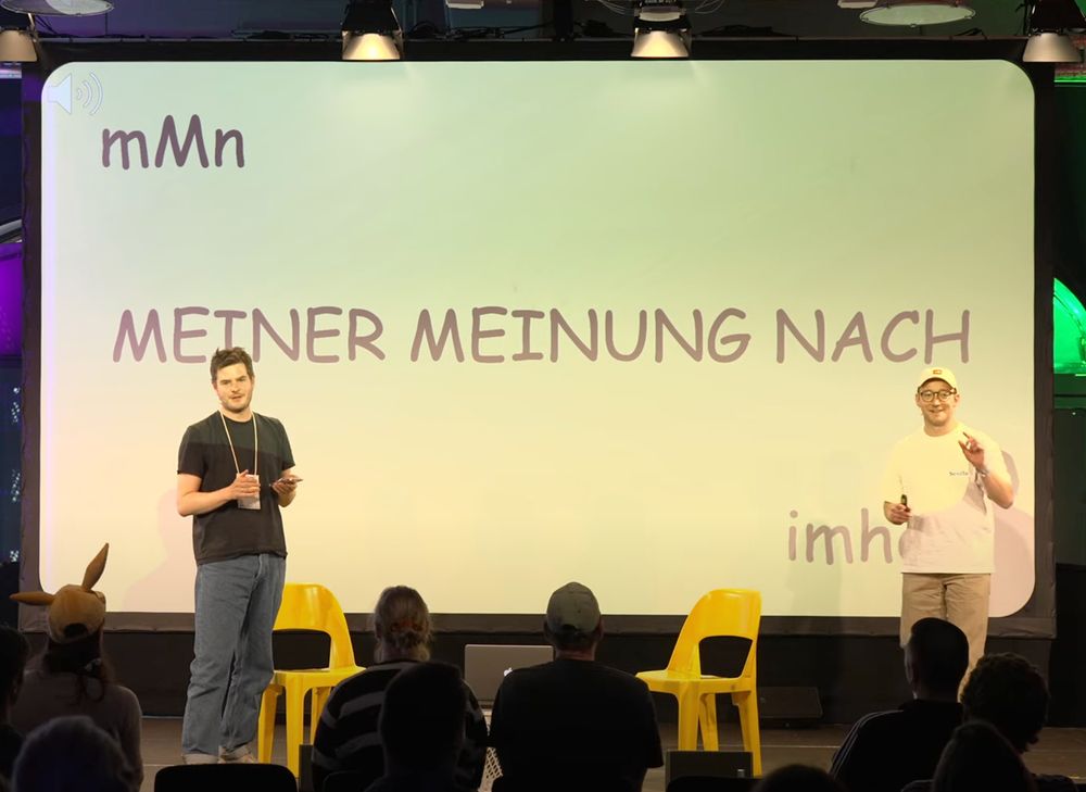 Dax und Moritz auf einer Bühne, auf der Leinwand hinter ihnen steht "mMn Meiner meinung nach imho"