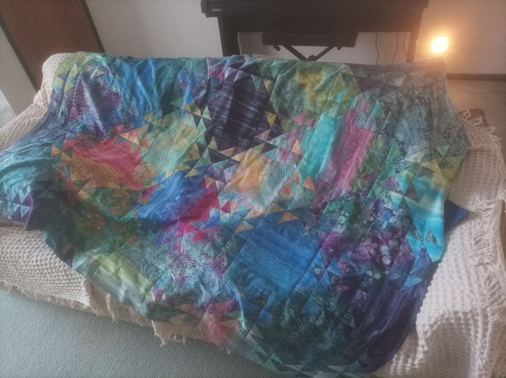 A colourful patchwork quilt top (in a "shimmer" pattern) draped over a sofa.