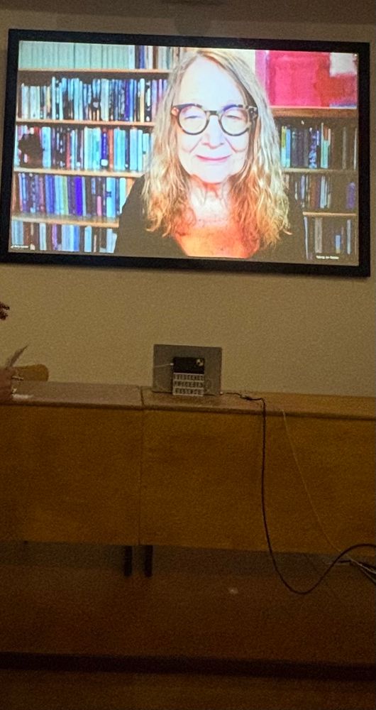Photo of Betty Cannon on a large screen (via Zoom) at the back of a stage, listening to a question from an audience member. 