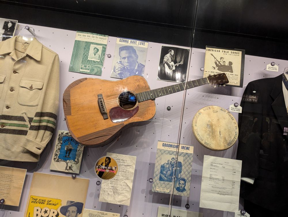 Elizabeth Cotten's old Martin acoustic guitar is hanging up on a museum display with clothes, pictures, and other music paraphernalia. Since she played it left-handed, it should be hanging the other way, but you can't win 'em all.