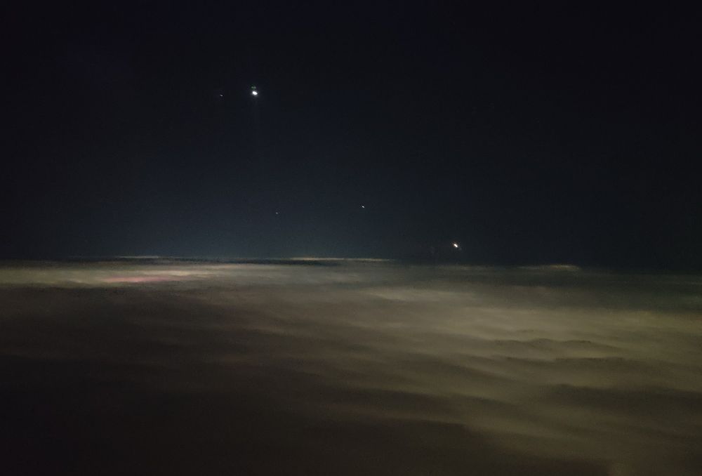 Photo from an aeroplane window of Venus (top left) and Mars (bottom right) above clouds illuminated from below by the lights of Manchester 