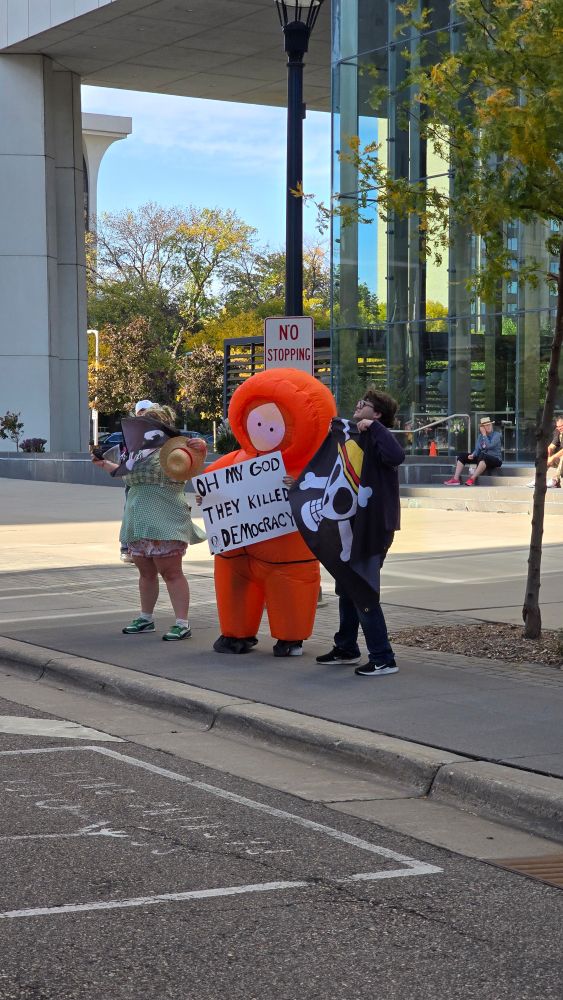 Kenny from South Park with a sign reading  "Oh my god, they killed democracy" 