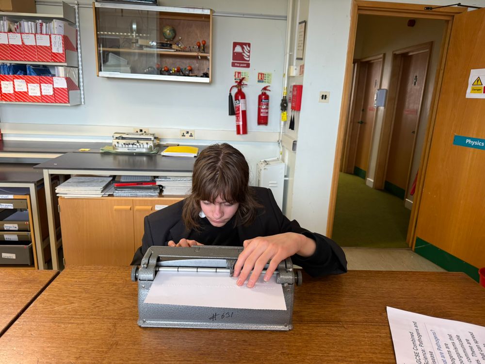 Photo of a student sat at a desk using a Perkins Brailler to write thank you notes 