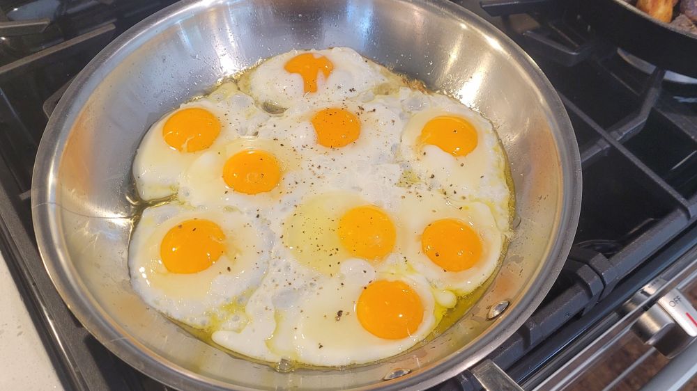 A frying pan filled with beautiful, fluffy eggs cooking over easy. Thr intensely yellow yolks are not yet cooked.