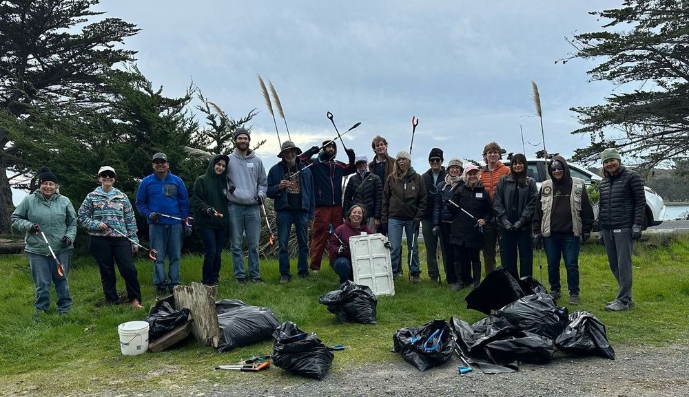 A group of volunteers gathered around several trash bags filled with plastic pollution and other debris they cleaned up.