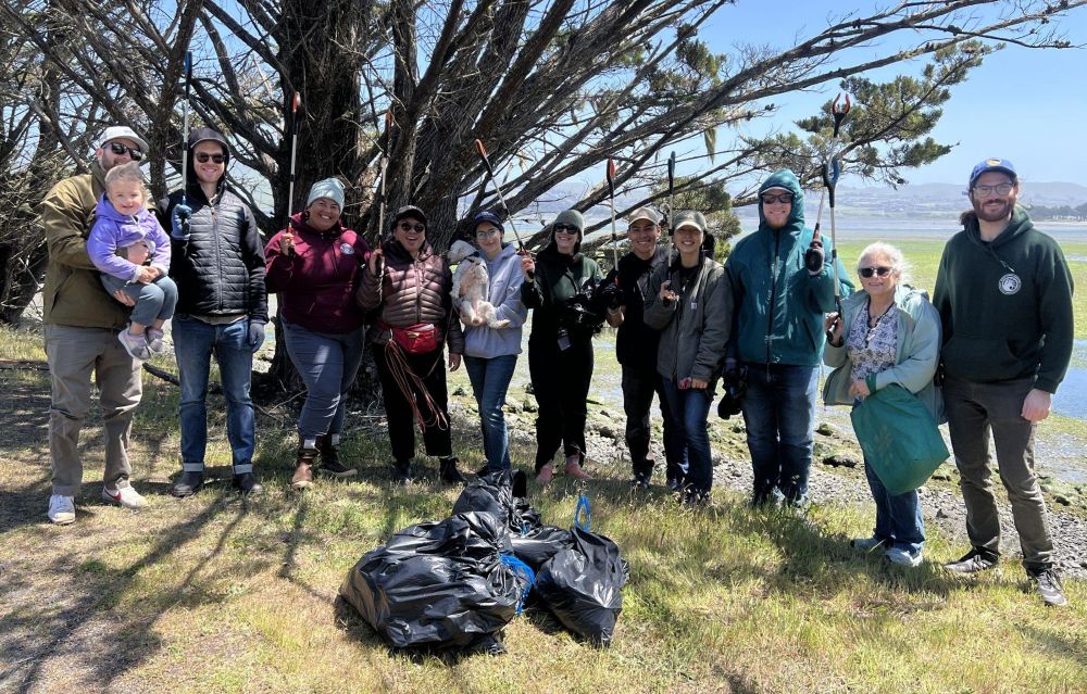 A group of volunteers gathered around several trash bags filled with plastic pollution they cleaned up.