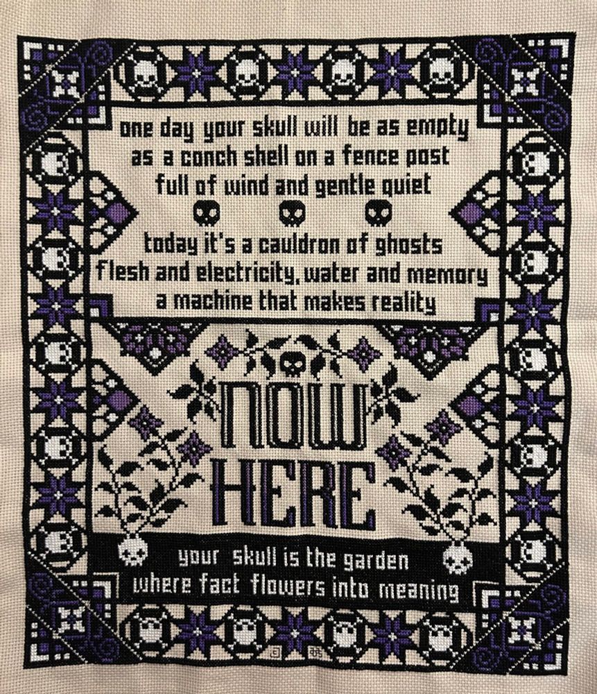 A black, white and purple cross stitch. There is a border of quilt stars and skulls, and it reads "one day your skull will be as empty as a conch shell on a fence post, full of wind and gentle quiet. Today it's a cauldron of ghosts flesh and electricity, water and memory, a machine that makes reality. Now, here, your skull is the garden where fact flowers into meaning."