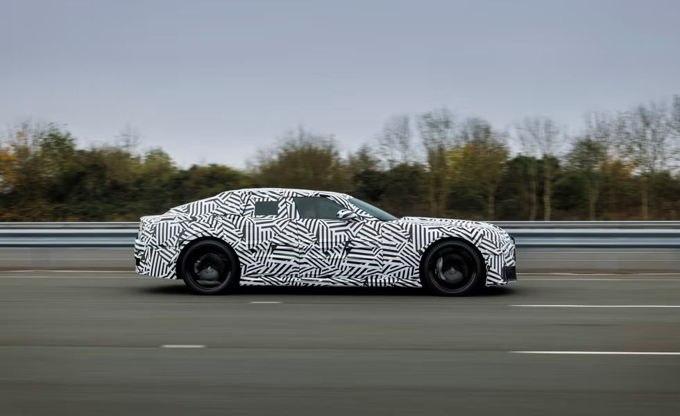 A photo of the new Jaguar "I-Type" being tested on a public road. It is heavily camouflaged in the way prototypes usually are, but is quite clearly a very ugly car.