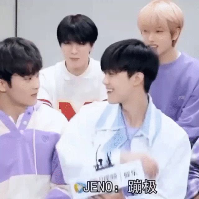 a group of young men are sitting next to each other and one of them is holding a piece of paper that says jeno .