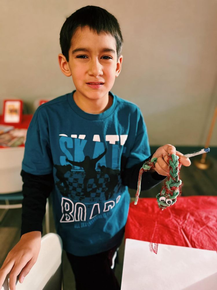 A child and the snake that they made with yarn and googly eyes.