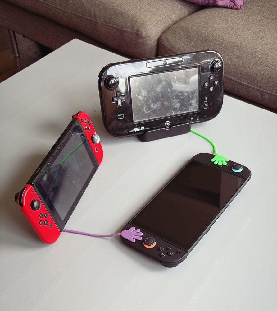 A WiiU and a Nintendo Switch with sticky hands touching a Nintendo Switch 2