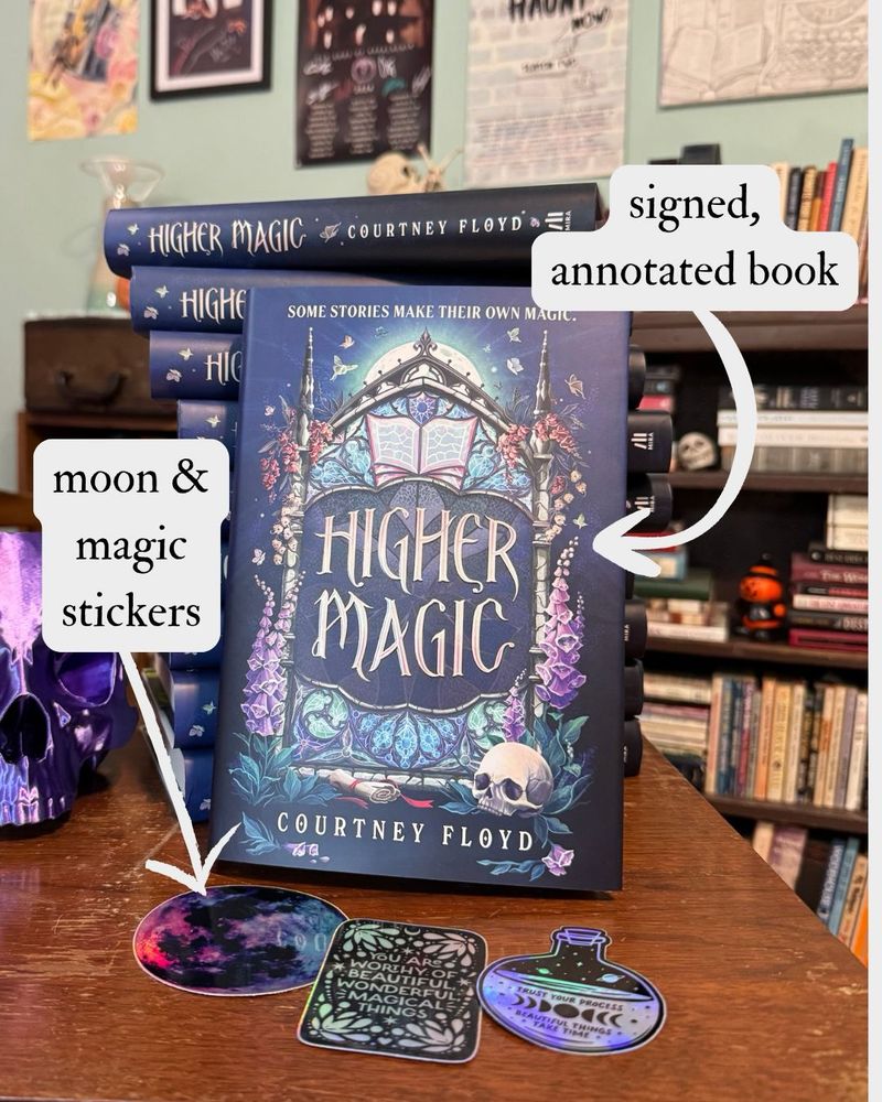 A signed, annotated copy of HIGHER MAGIC propped up against a stack of other copies of HIGHER MAGIC with some moon- and magic-themed stickers. 