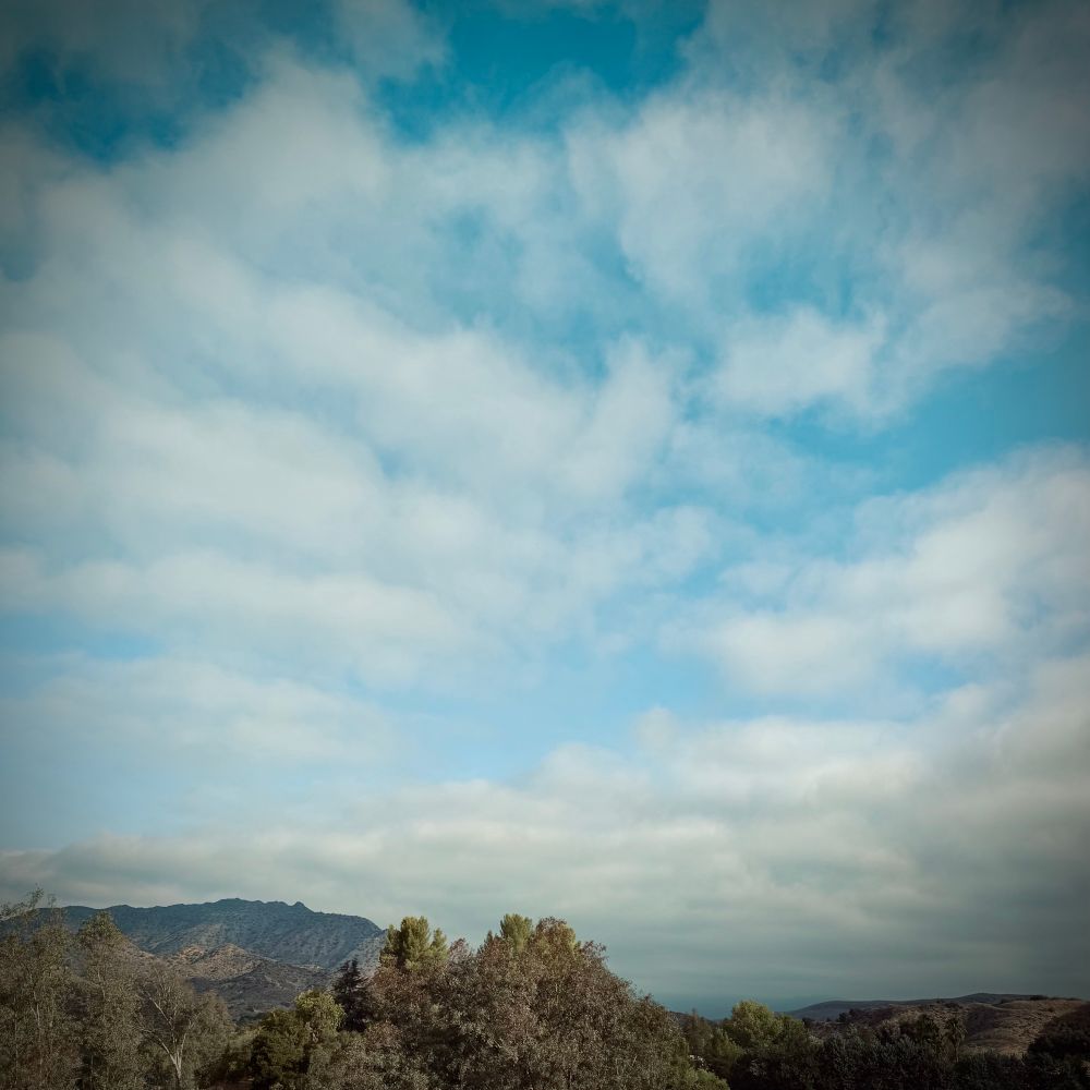 Lots of soft-looking gray clouds fill the sky with pockets of blue showing through. Lady Face Mountain ridgeline silhouetted on the right with trees and other hills filling in across the bottom. 