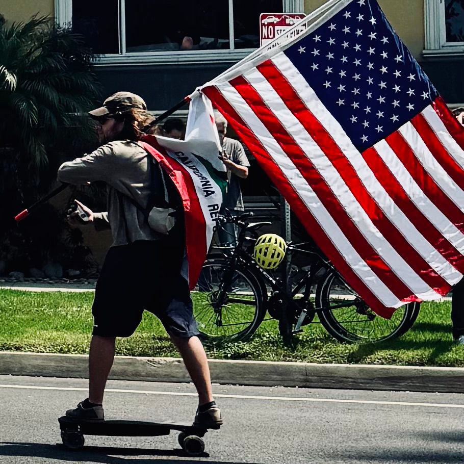 Skateboarder on Ocean Blvd with US flag and California state flag. 