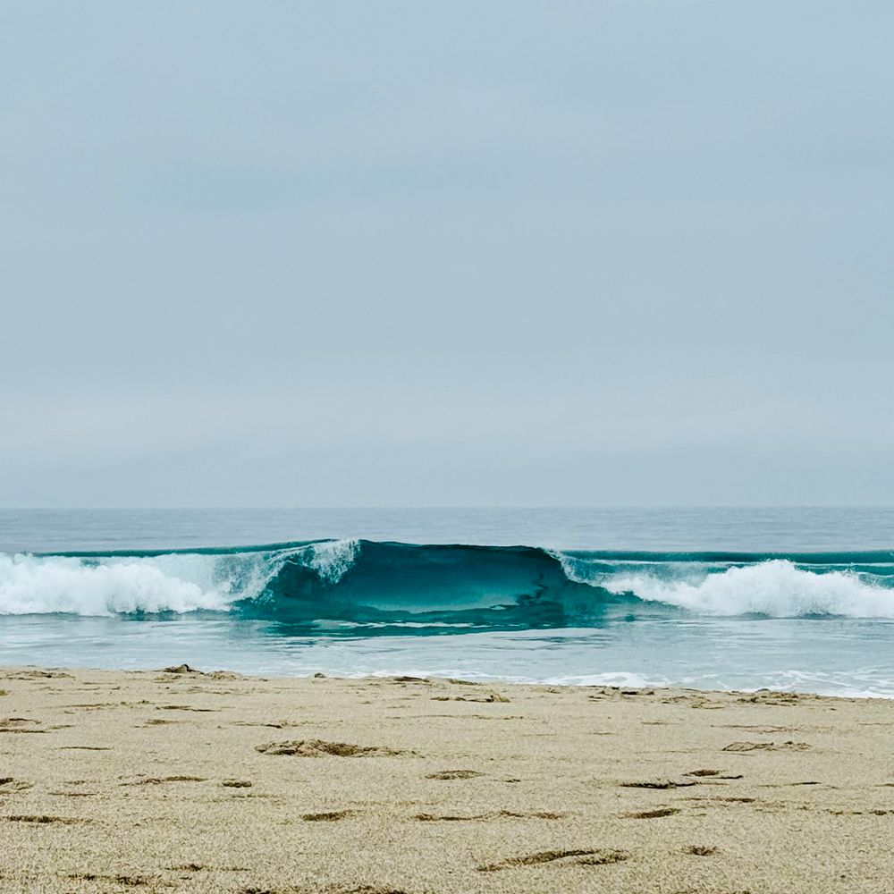 Vivid sea green waves crashing onto shore. Foggy sky behind the Pacific. 