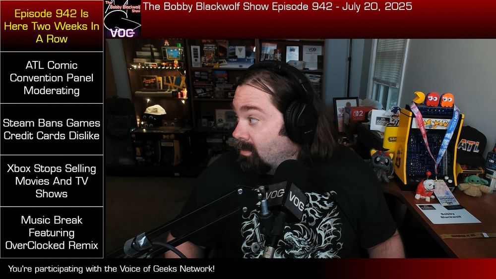 A screengrab from this past Sunday, July 20, 2025, of me wearing an SGDQ t-shirt, looking to the left at headlines for the evening on the Twitch stream. The mic is on a mic arm and has a VOG Network mic flag on it (where I broadcast now) - but is actually still a Shure C608 from 2005. (I have five of them, just in case one goes out!)