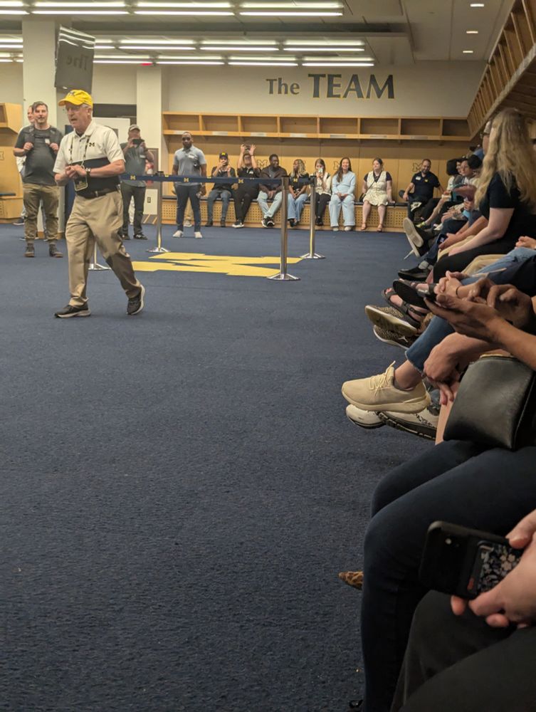 A group of people sit in the Michigan Stadium locker room 