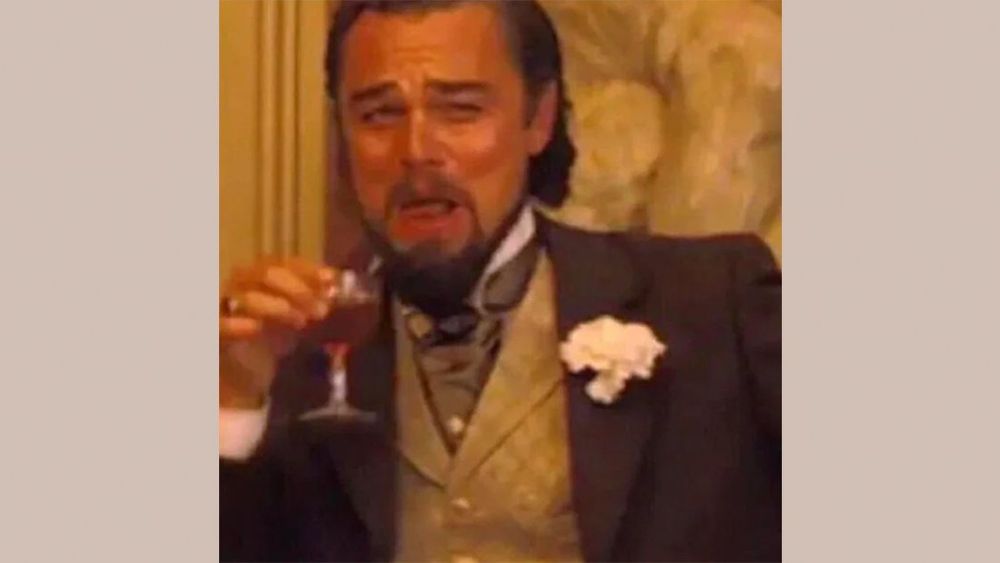Leonardo DiCaprio in seiner Rolle in Django Unchained im Anzug mit Weste hält ein Gläschen Alkohol und lacht dabei