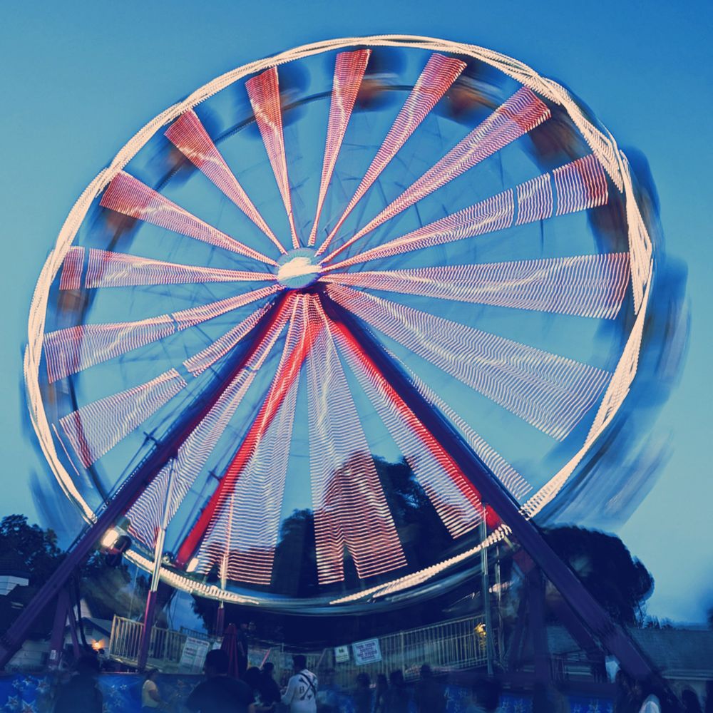 The same Ferris Wheel, a little later and a bit darker. Again, a long exposure is used to blur motion into a series of spokes with a jagged rim of light.