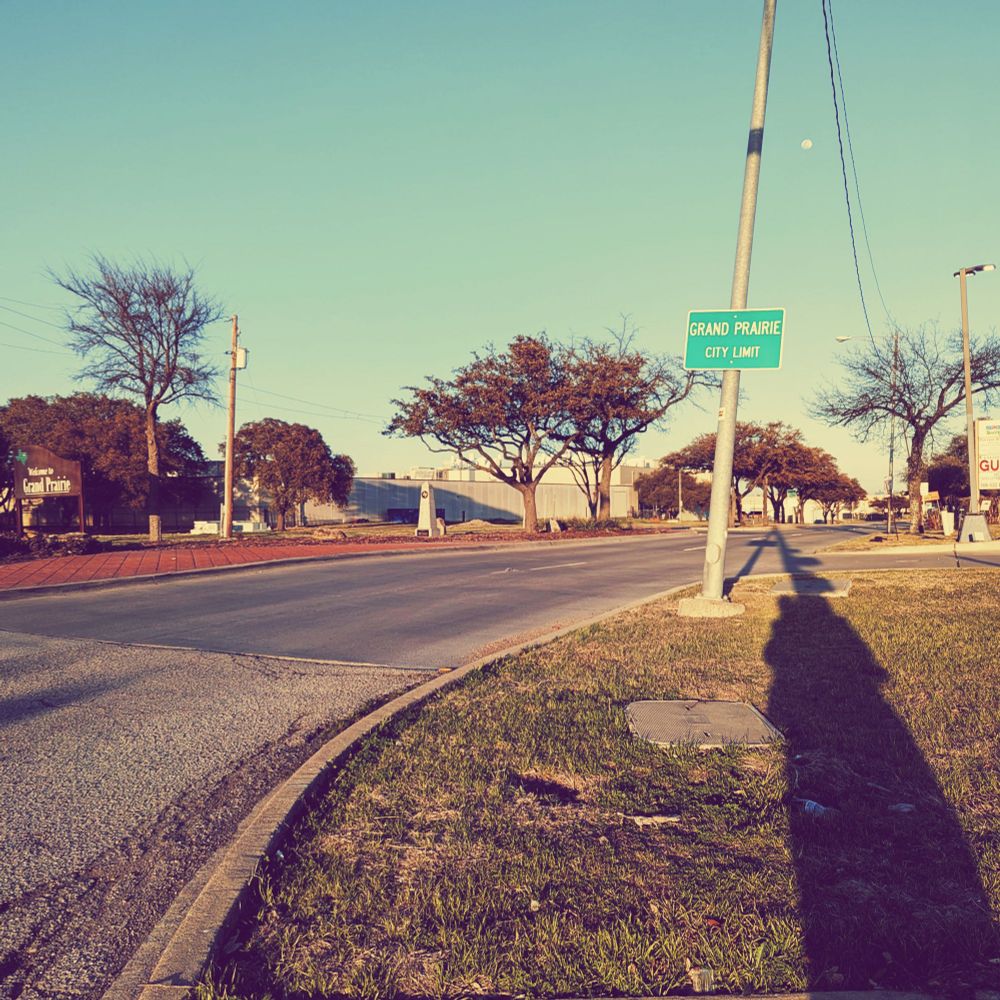 Signs welcoming drivers to Grand Prairie, Texas, including a city limits sign. Although there is room, there are no sidewalks in this picture.