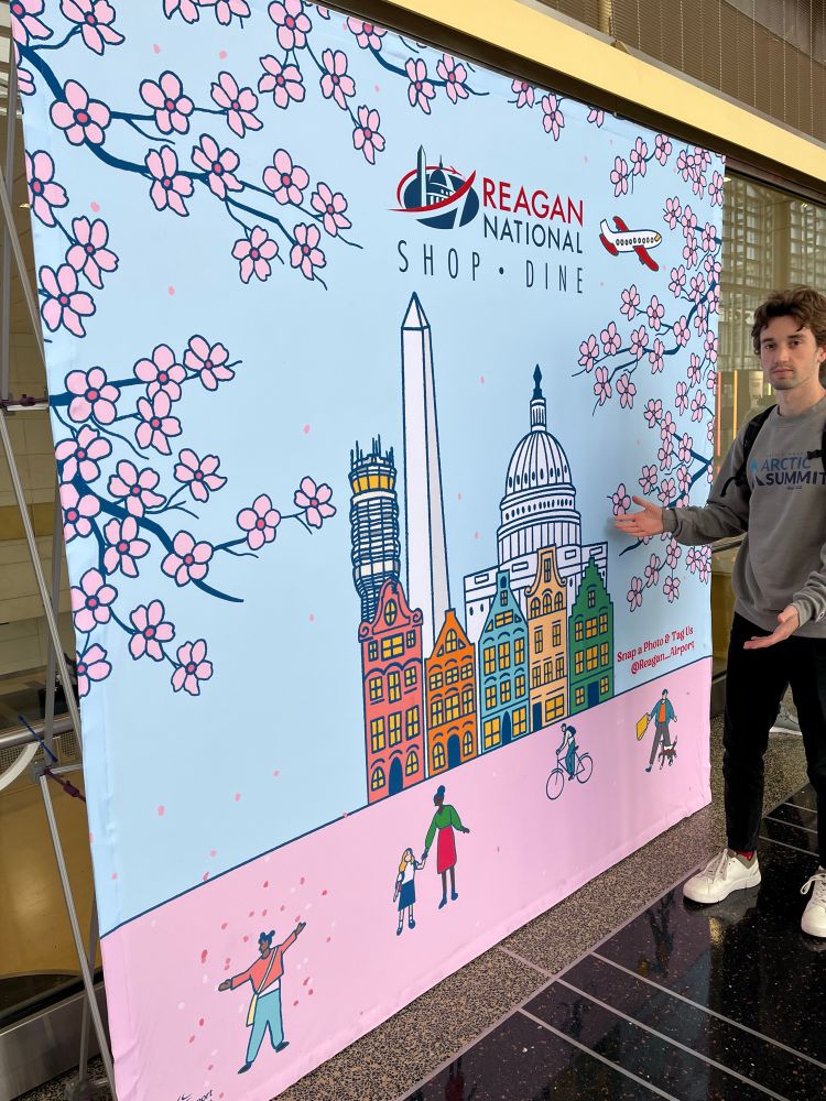 me posing in front of a condensed DC poster which features row homes, the washington monument, and the capitol
