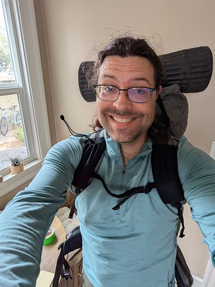 Selfie of Aaron in his kitchen wearing a backpacking pack and a slightly nervous smile.