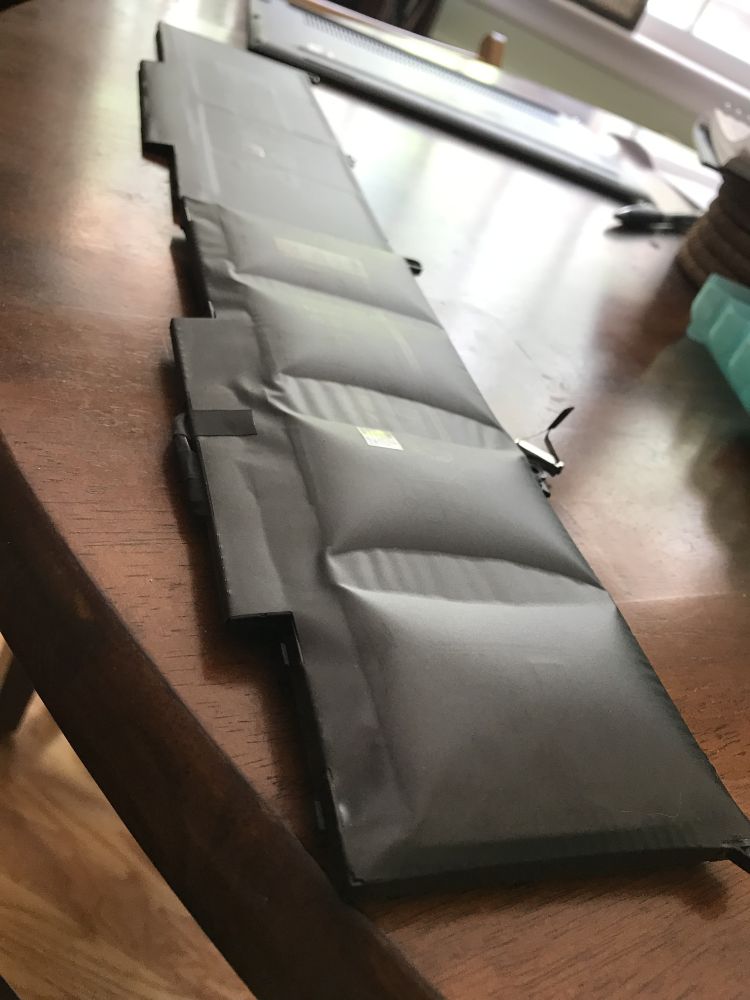 Two laptop batteries, in the background, a normal laptop battery, in the foreground, a spicy laptop battery that has expanded significantly. 