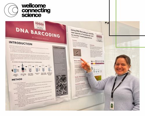 A woman stood smiling and pointing at a DNA Barcoding poster the students have made