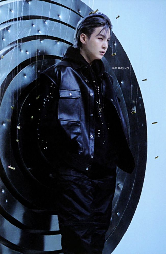 Yoongi in one of the Proof promotional photos. He's standing in front of a bullseye image with bullets around him. He's wearing all black and looks like a dream.