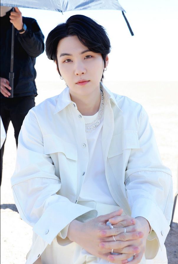 Yoongi all in white, hands clasped over crossed knees, black hair, side part, swept to the side, looking straight at the camera aka straight at Army.  Silver chains, earrings, rings complete his look (of devastation...this pic is almost too much. Something about how he makes eye contact like this...!)