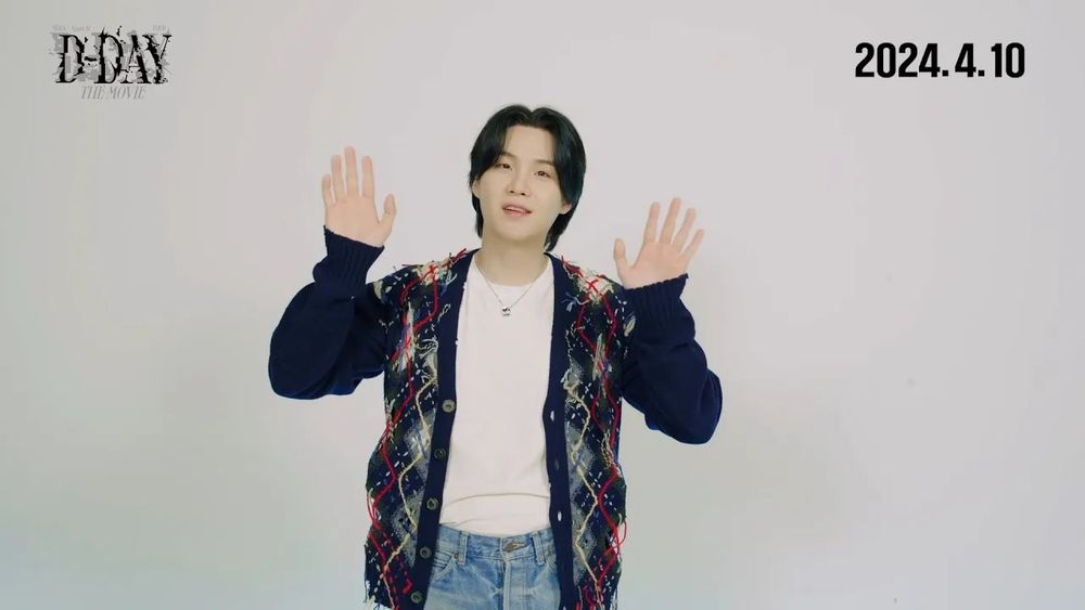 Black haired Yoongi with his hands up, wearing jeans, white shirt and a black and argyle Dad cardigan :). 