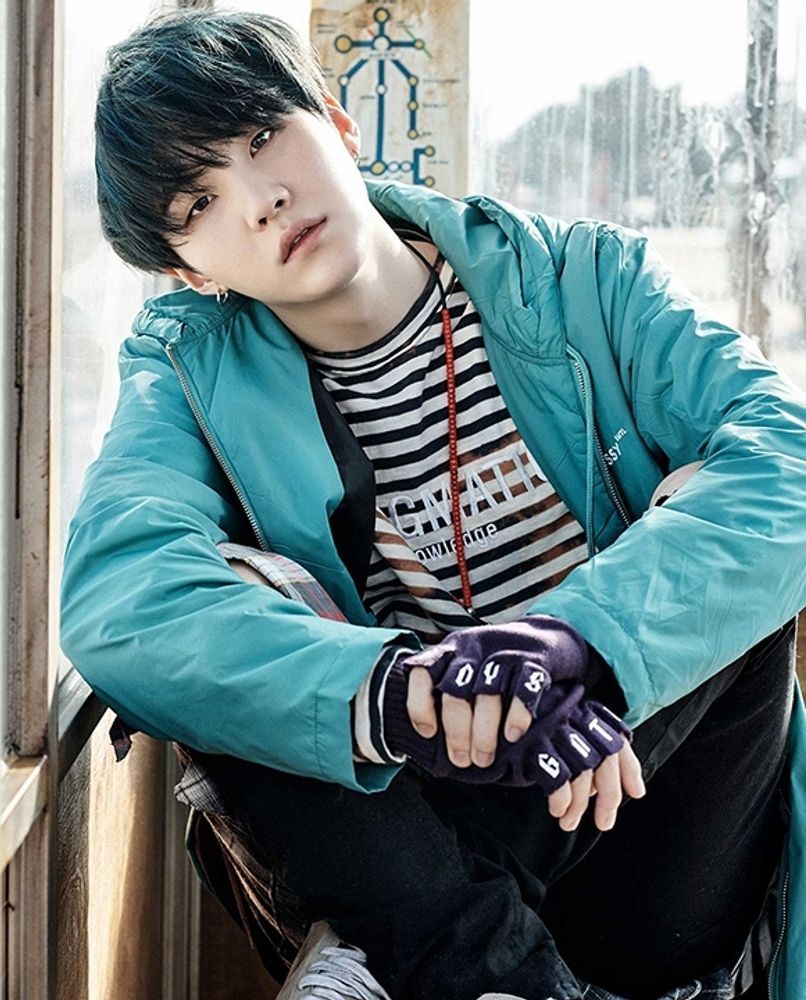 This is the very first pic of Yoongi I ever saved.  I have such affection for it. He has black hair, is wearing a black and white striped shirt with a turquoise jacket over it, and fingerless gloves. He is sitting, smol and looking a little serious, leaning against a window.  Just very fond of this pic!!  It is such a mood. 