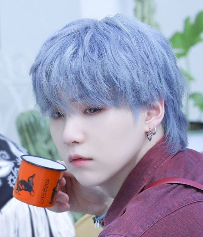 Blue Yoongi from a PTD Behind shot (cropped to focus on his pretty face).  Blue hair, burgundy red/orangeish shirt (how to describe that color, huh?), He is sipping from a tiny red with black SNOB (lol) tin(?) coffee mug.  Drinking who knows what.  He is actually looking at someone holding a script in their hand.  I believe that is JK to the background?  And behind him, big green leaves.  :) 