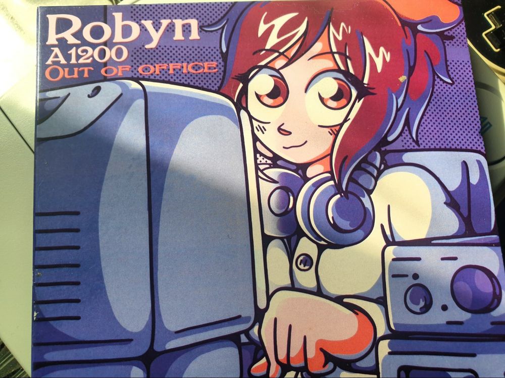 A photo of cute digipak giver with an illustration of a smiling anime-ey gal wearing neck-slung headphones sat at a crt monitor next to audio equipment. 