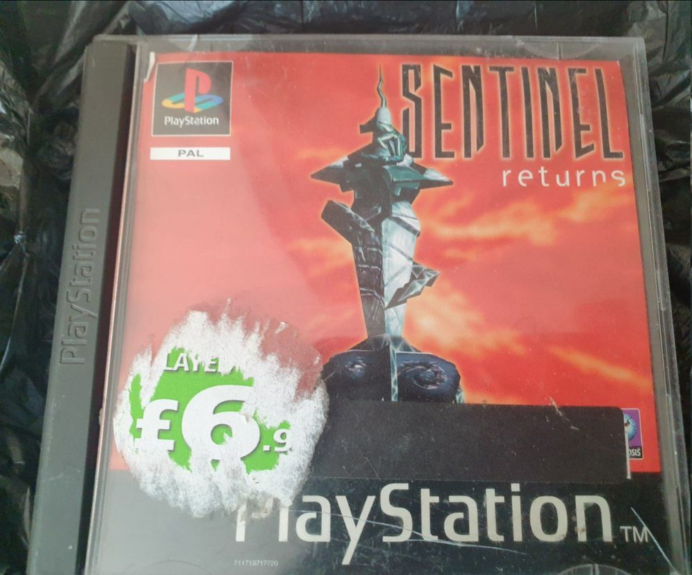 A photo of Sentinel Returns for PS1's PAL release case on top of a black plastic bin bag that apparently provides more comfort to a cat than a plush cushion.