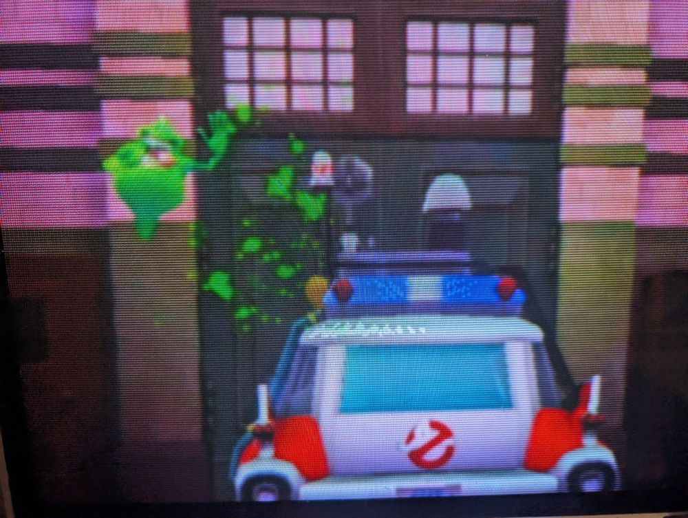 A crt TV screenie with Ecto-1 in the station house and Slimer floating above it.