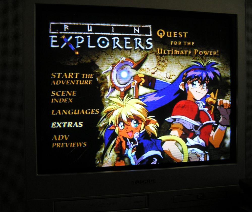 A 2004 Olympus digi-cam photo of our Toshiba flatscreen crt tv with the ADV DVD release of Ruin Explorers' title screen with the main two protags, a blue haired warrior and catgirl mage, posed with the options to the left of them.