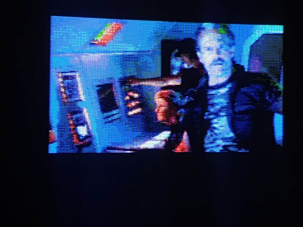 A crt TV screenie of one of live action Night Trap's cinematics with the moustached unit commander briefing you in a control centre  