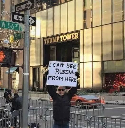 guy holding up sign in front of trump tower that says 'i can see russia from here'