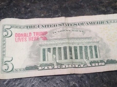 a 5 dollar bill - the side with the lincoln memorial on it and someone stamped - donald trump lives here with an arrow towards it