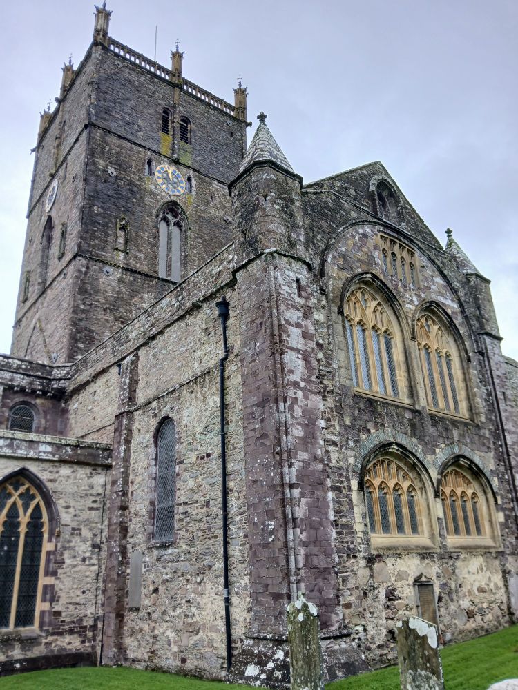 Cathedral towers with windows tower in front. Ancient cathedral of stone. Arched brown framed windows in towers. A little bit of lawn in front, cloudy sky behind.