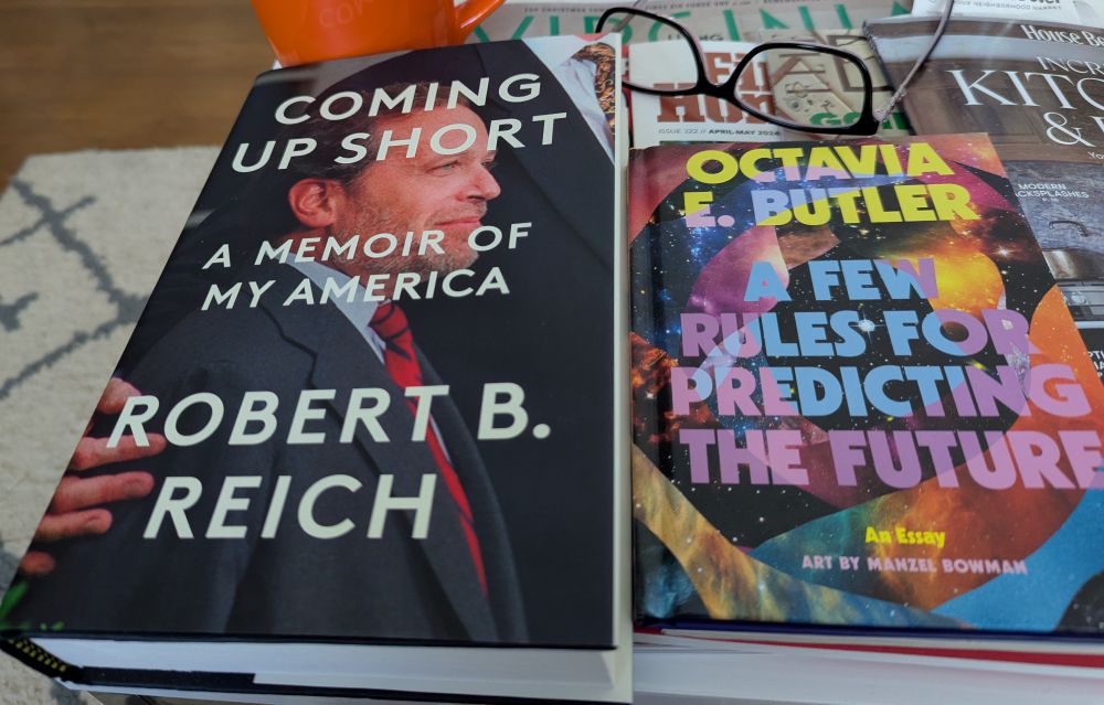 A pair of reading glasses with books from left to right: Coming Up Short A Memoir of My America Robert B. Reich, Octavia E. Butler A Few Rules for Predicting the Future An Essay Art by Manzel Bowman