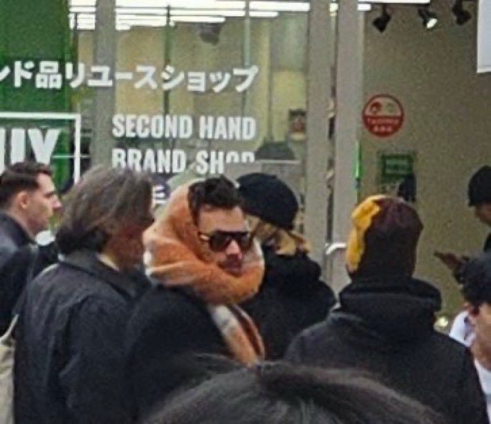 Shot of Harry styles wearing an oversized orange scarf wrapped around his head and neck, showing mostly just his forehead, mustache, and an enormous pair of sunglasses
