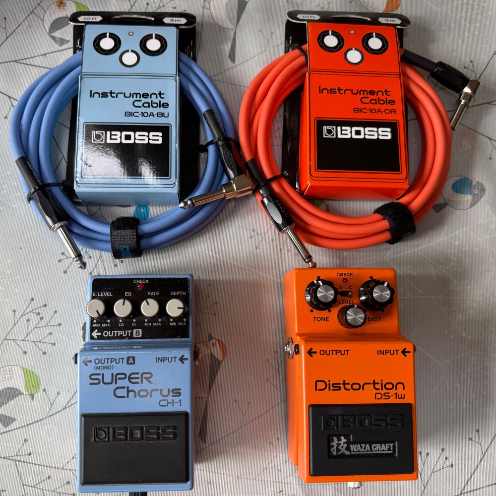 The same two cables as in the previous picture but now each one is next to its matching guitar pedal. The blue cable is next to a Boss Super Chorus CH-1 and the orange cable is next to a Boss Waza Craft Distortion DS-1w. 