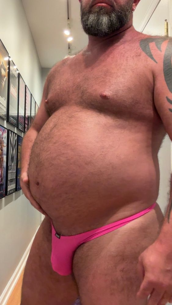 A hairy musclechub shows off his swollen belly in a pink g-string