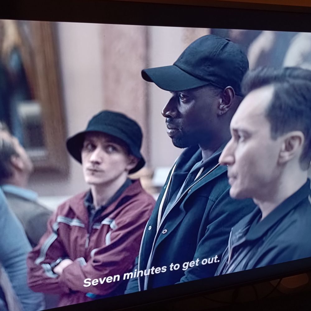 A still from the series Lupin. Lupin is in the middle and the subtitle says seven minutes to get out