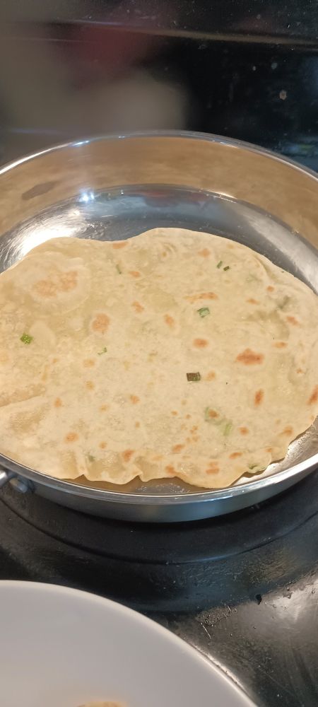 A flat tortilla cooking in a pan with specks of brown from the top side already having been fried 