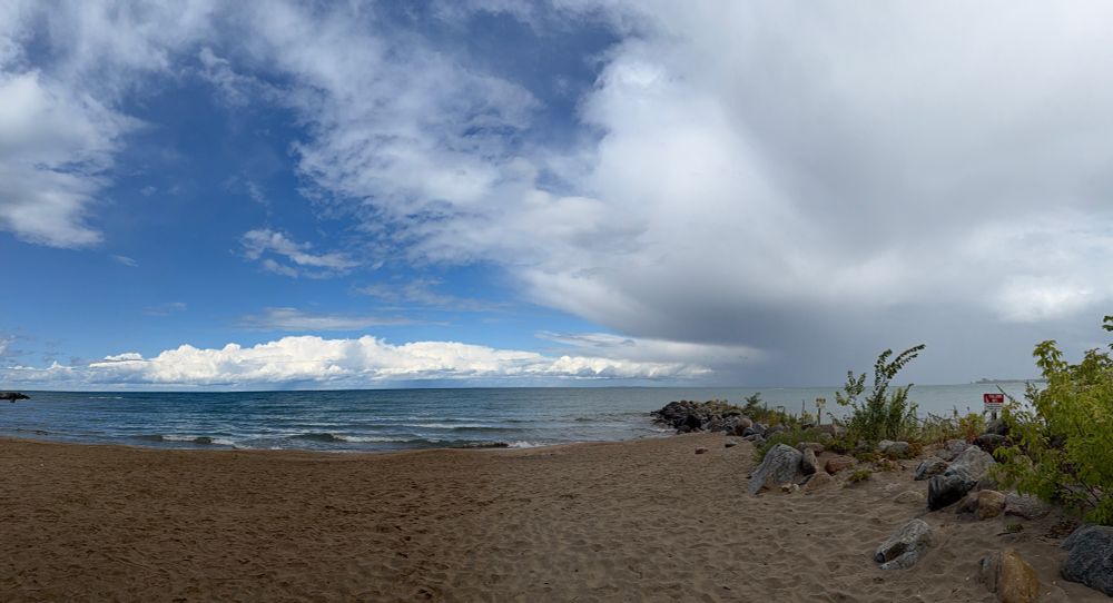 Beach landscape with bright white clouds in a blue sky being quickly overtaken by large rainclouds. 